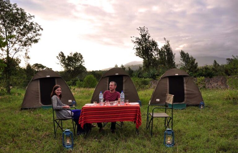 Two tourists having dinner outdoors in a public campsite with their tents behind them