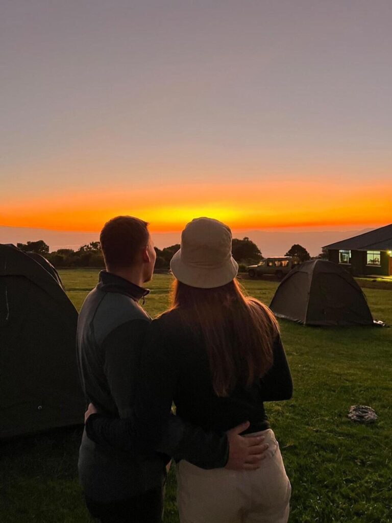 a couple watching the sunset om their public campsite full of tents in Ngorongoro