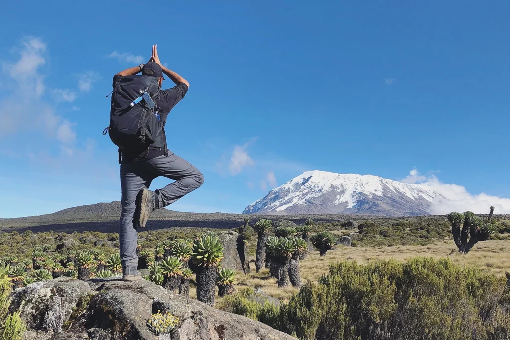 a hiker doing a yoga pose while facing Mt. Kilimanjaro via the Marangu route